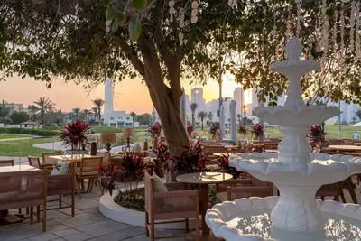 Cane chairs and tables around a white stone fountain on the terrace at Address Montgomerie