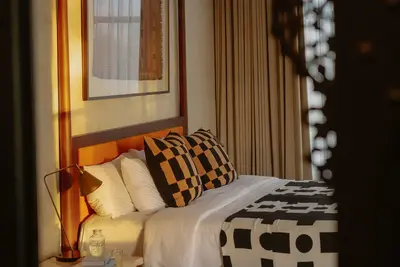 A timber four poster bed with a brass lamp and patterned cushions at Rumah Buaya