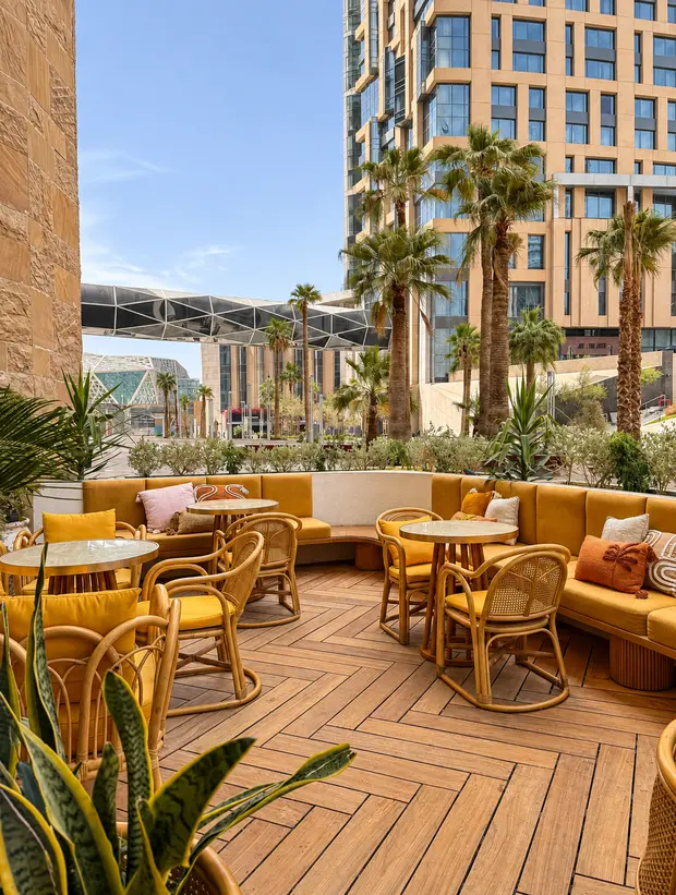 Yellow banquettes and rattan chairs on the terrace at KAFD, the district towers behind