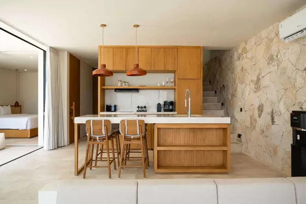 Una isla de cocina de madera y taburetes contra un muro de piedra en Ohana Villa