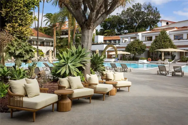 Cushioned daybeds under a mature tree beside the pool at Radisson Resort and Residences, Tenerife