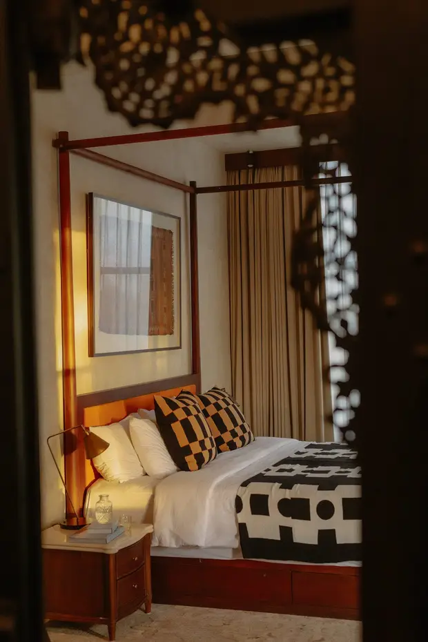 Una cama con dosel de madera, lámpara de latón y cojines estampados en Rumah Buaya